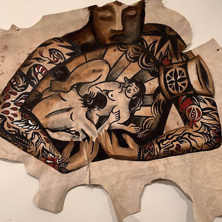 Painting on leather, uses bold lines, black ink, red ink, and some white. A tattooed person holds a vase. On the vase is an image of two women performing cunnilingus.